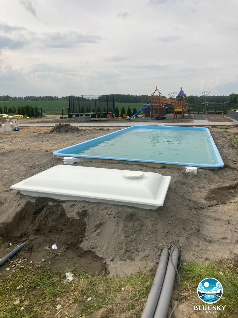 Basen betonowy z niebieską folią podczas budowy z białym zbiornikiem techniki basenowej