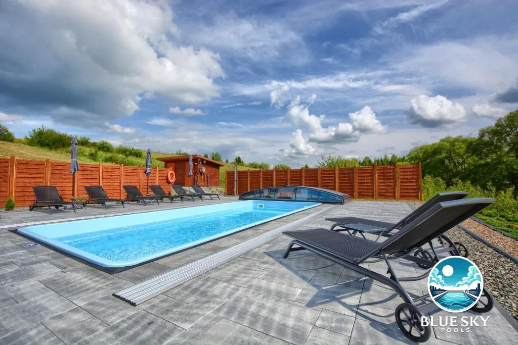 Basen hotelowy z niebieską folią, leżaki, drewniane ogrodzenie i zadaszenie basenowe